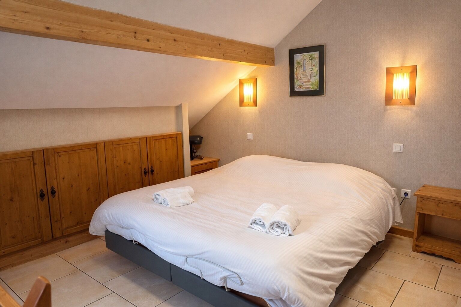 A bedroom with a large bed, wooden wardrobe, and two wall-mounted lights.