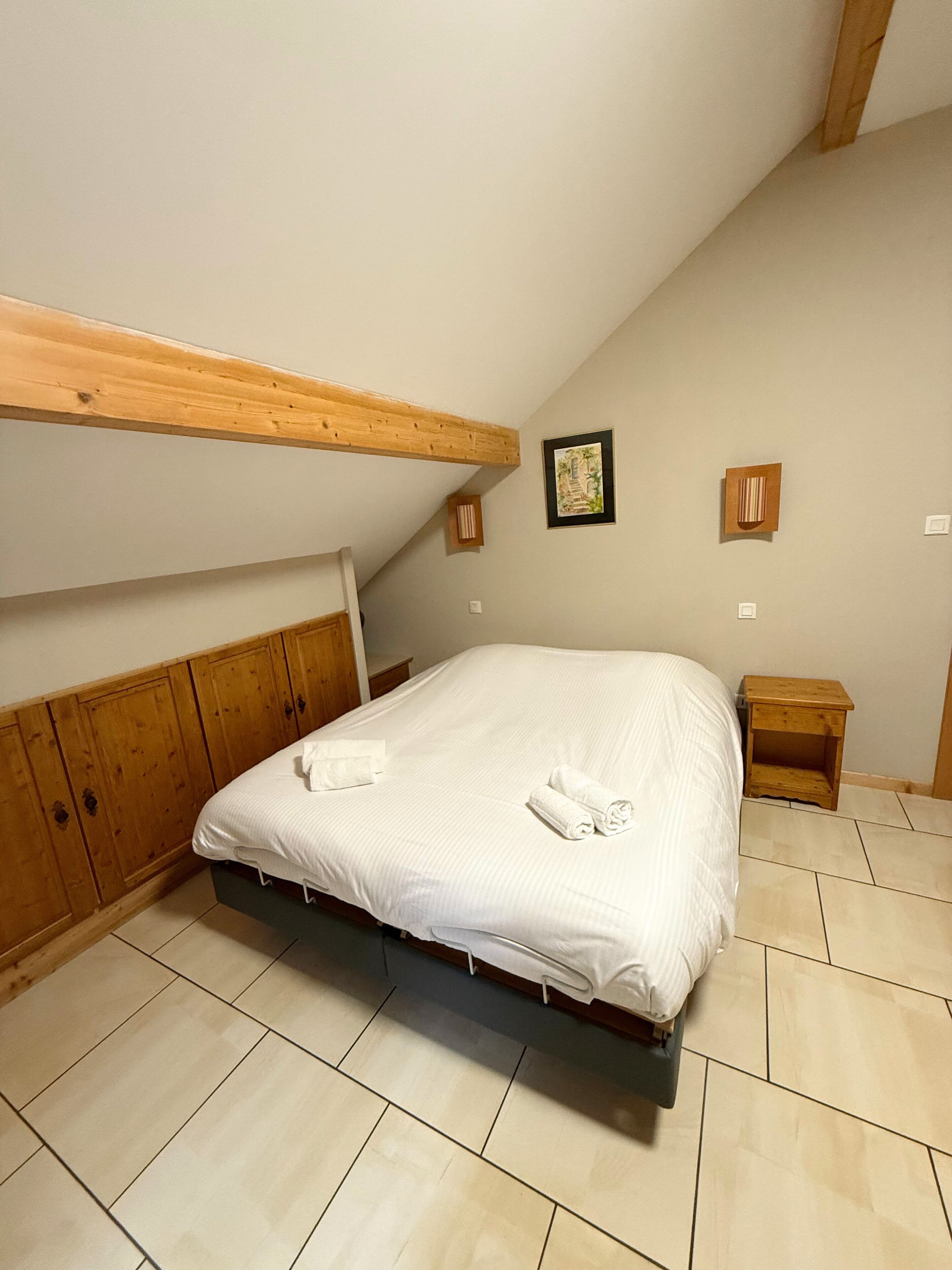 A bedroom with a wooden headboard, a bed with white linens, a small wooden nightstand, and a framed picture on the wall.