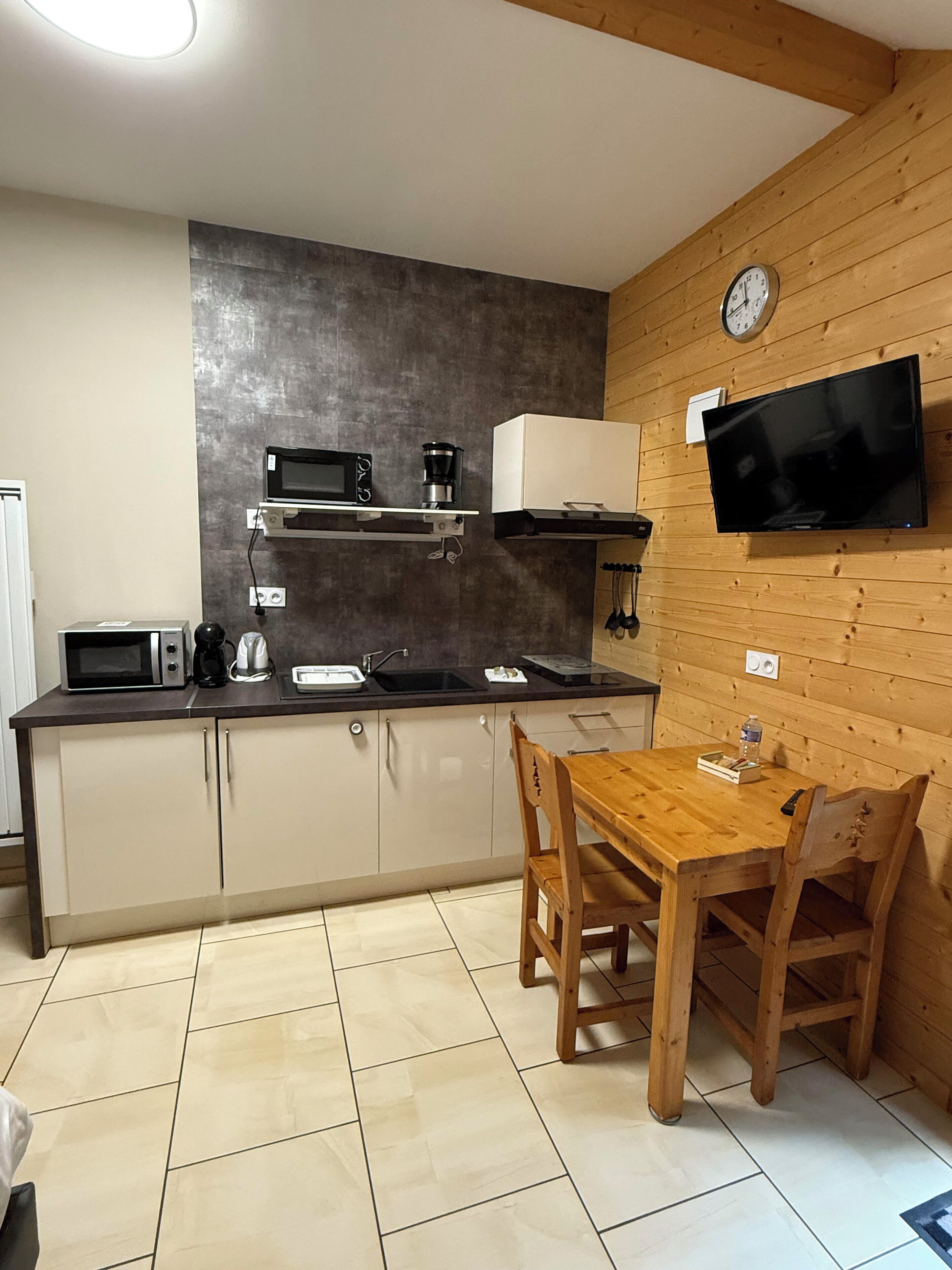A compact kitchen with a microwave, coffee maker, and a TV mounted on the wall.
