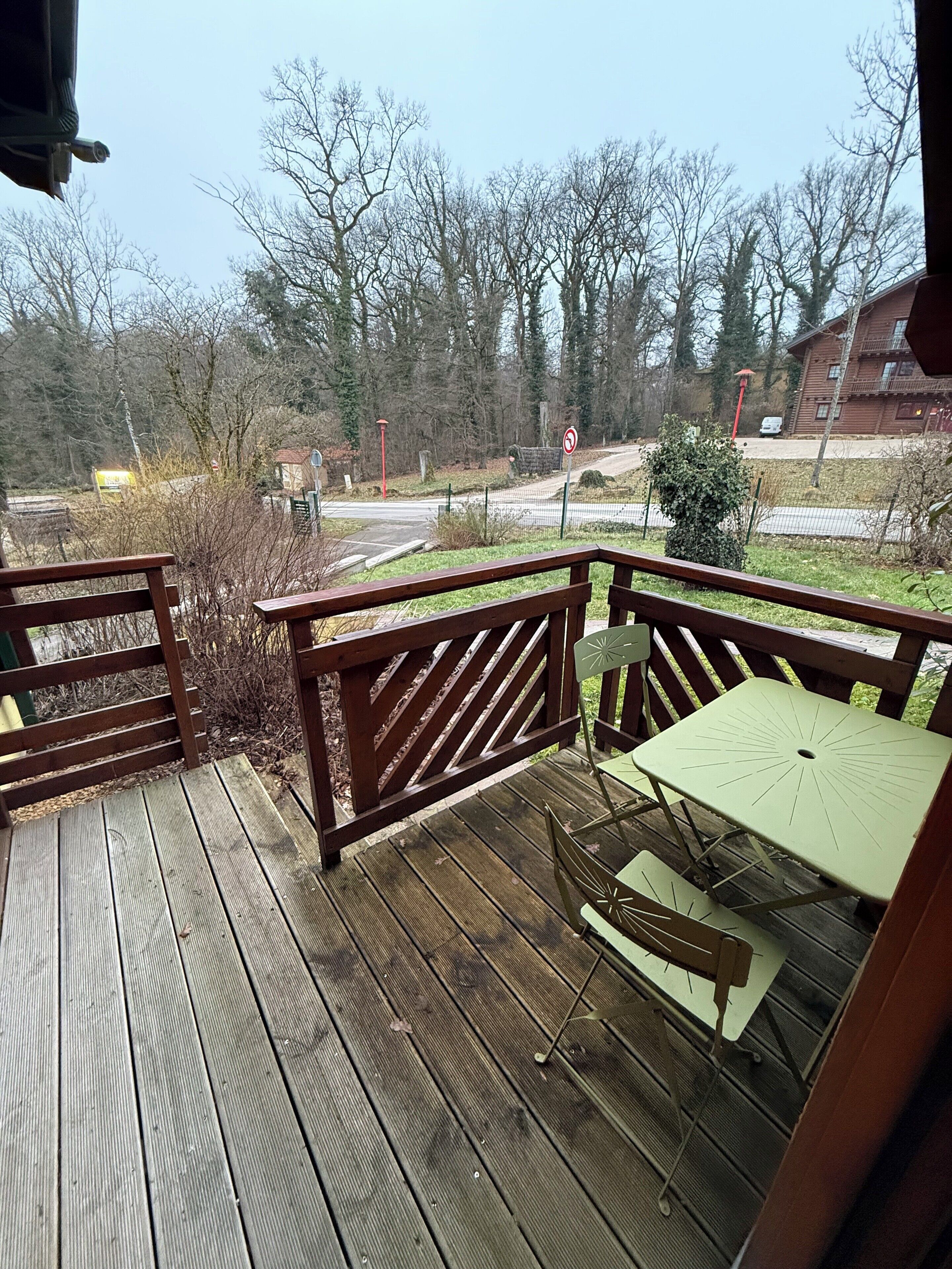 Eine Holzterrasse mit Tisch und Stühlen, mit Blick auf eine Straße und Bäume.