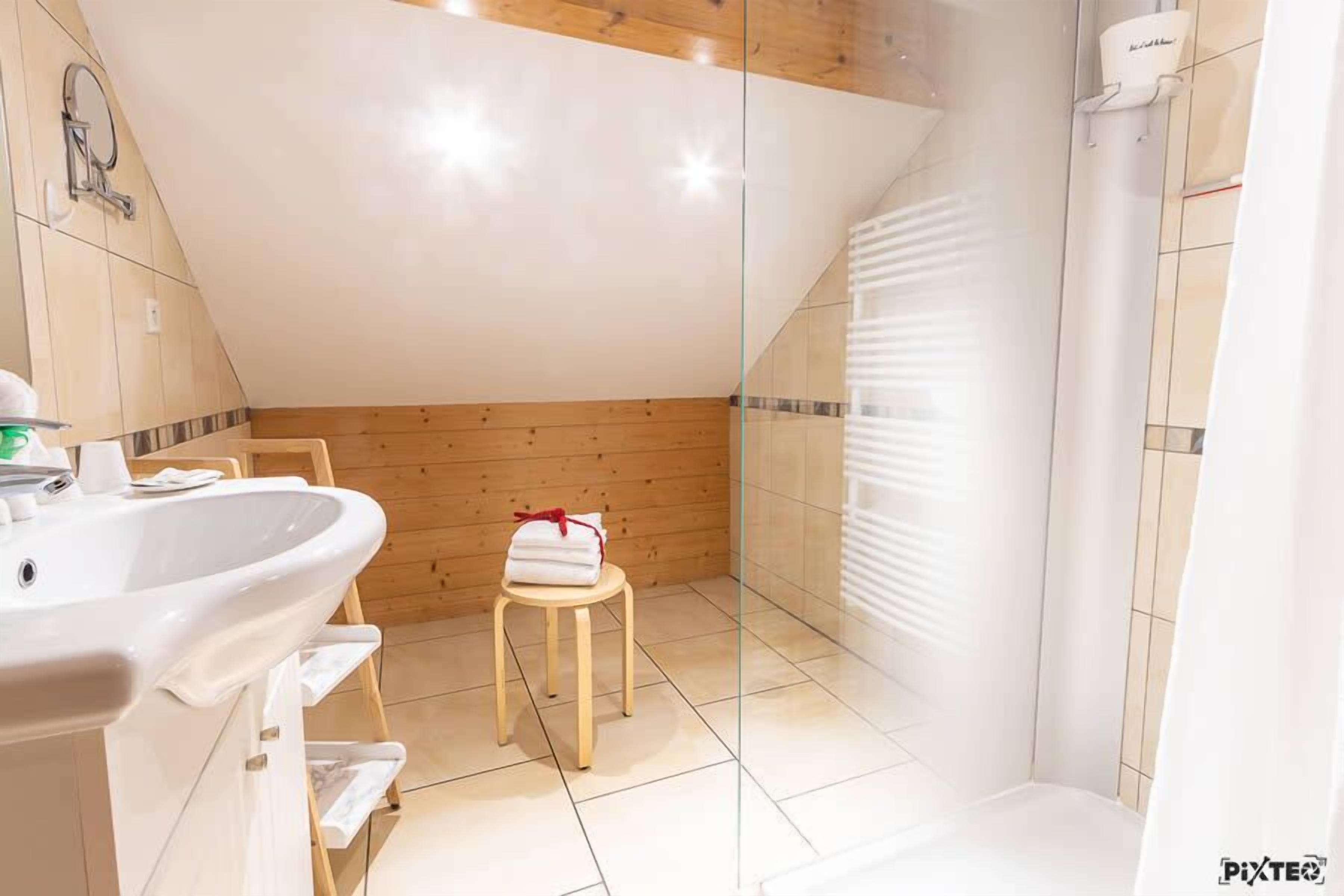 Un baño moderno con techo de madera, lavamanos blanco y cabina de ducha de vidrio.