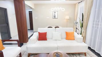 Una sala de estar moderna con un sofá blanco, cojines rojos y blancos, una mesa de centro de madera y una lámpara fijada a la pared.