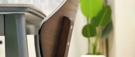A chair with a wooden backrest and metal frame, positioned in a room with a potted plant and a white wall.