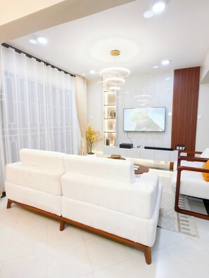 A modern living room with a white sofa, a flat-screen TV mounted on the wall, and a wooden accent wall. - Charm Luxe Homes (Kampala)