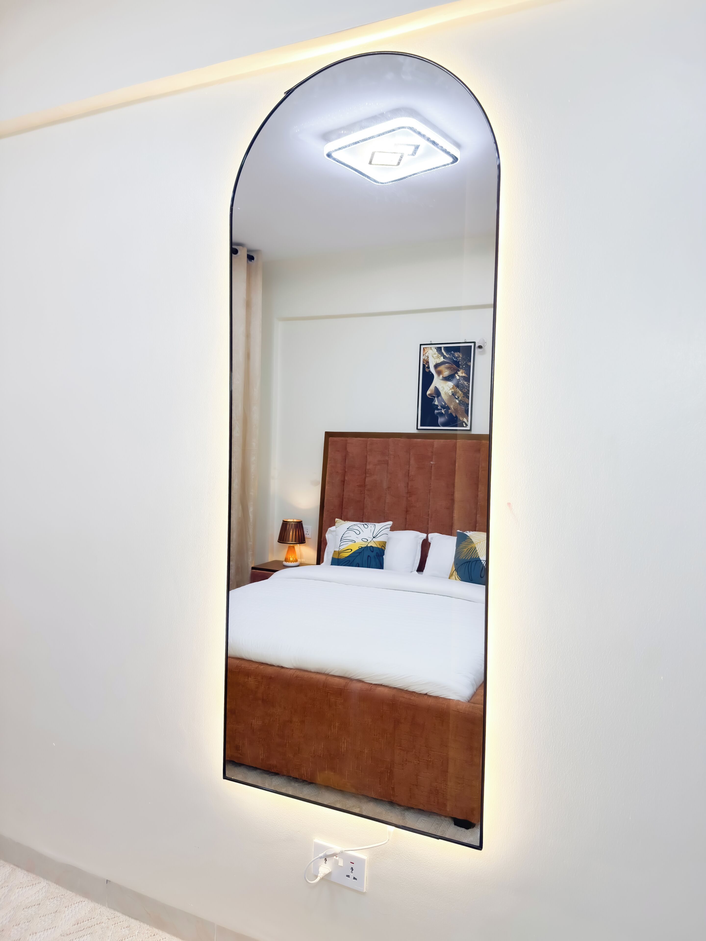 A bedroom with a bed, a nightstand, a lamp, a wall-mounted mirror, and a painting on the wall.