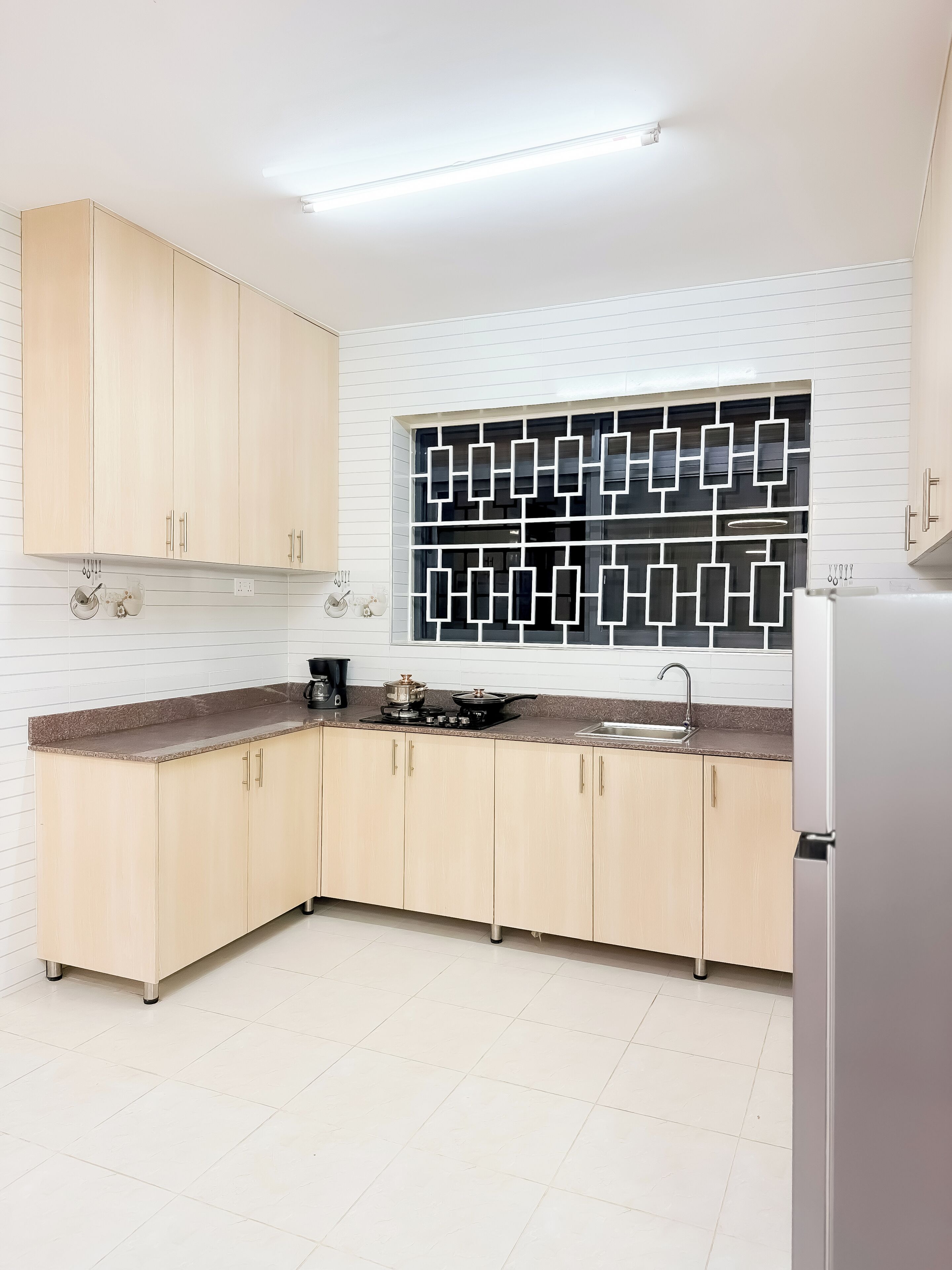 A modern kitchen with light wood cabinets, a black and white backsplash, and a stainless steel refrigerator.