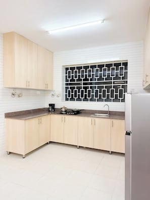 A modern kitchen with light wood cabinets, a black and white backsplash, and a stainless steel refrigerator. - Charm Luxe Homes (Kampala)