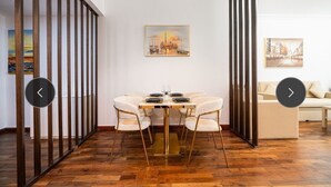 Een eetgedeelte met een ronde tafel, zes stoelen en een schilderij aan de muur.