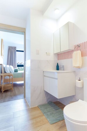 Un baño moderno con inodoro, lavamanos y espejo. Se ve una cama con vistas al exterior.