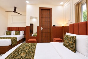 A hotel room with two beds, a wooden door, a ceiling fan, and a window with curtains. - SG Royal Portico (Haridwar)