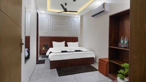 A modern hotel room with a large bed, a ceiling fan, an air conditioning unit, and a wooden bookshelf. - SG Royal Portico (Haridwar)