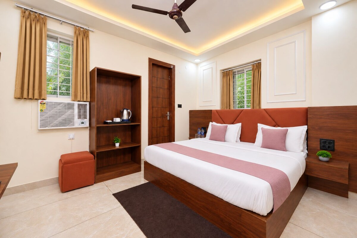 A hotel room with a large bed, a ceiling fan, an air conditioning unit, a small table, and a trash bin.