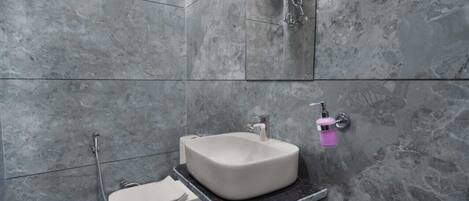 A bathroom with a marble floor, a white sink, a toilet, and a shower.