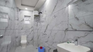 A modern bathroom with a marble floor and walls, a white toilet, a shower with a handheld showerhead, and a freestanding bathtub. - SG Royal Portico (Haridwar)