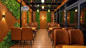 A restaurant interior with wooden paneling, green plants, leather seating, and pendant lighting.