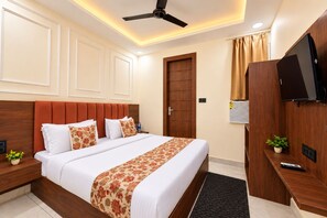 A hotel room with a bed, a TV, a ceiling fan, and a wooden wardrobe. - SG Royal Portico (Haridwar)