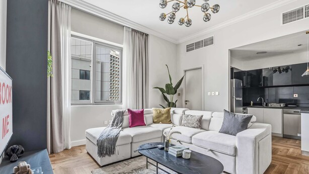 Una sala de estar moderna con un sofá blanco, una mesa de centro negra y vistas de la ciudad a través de grandes ventanales.