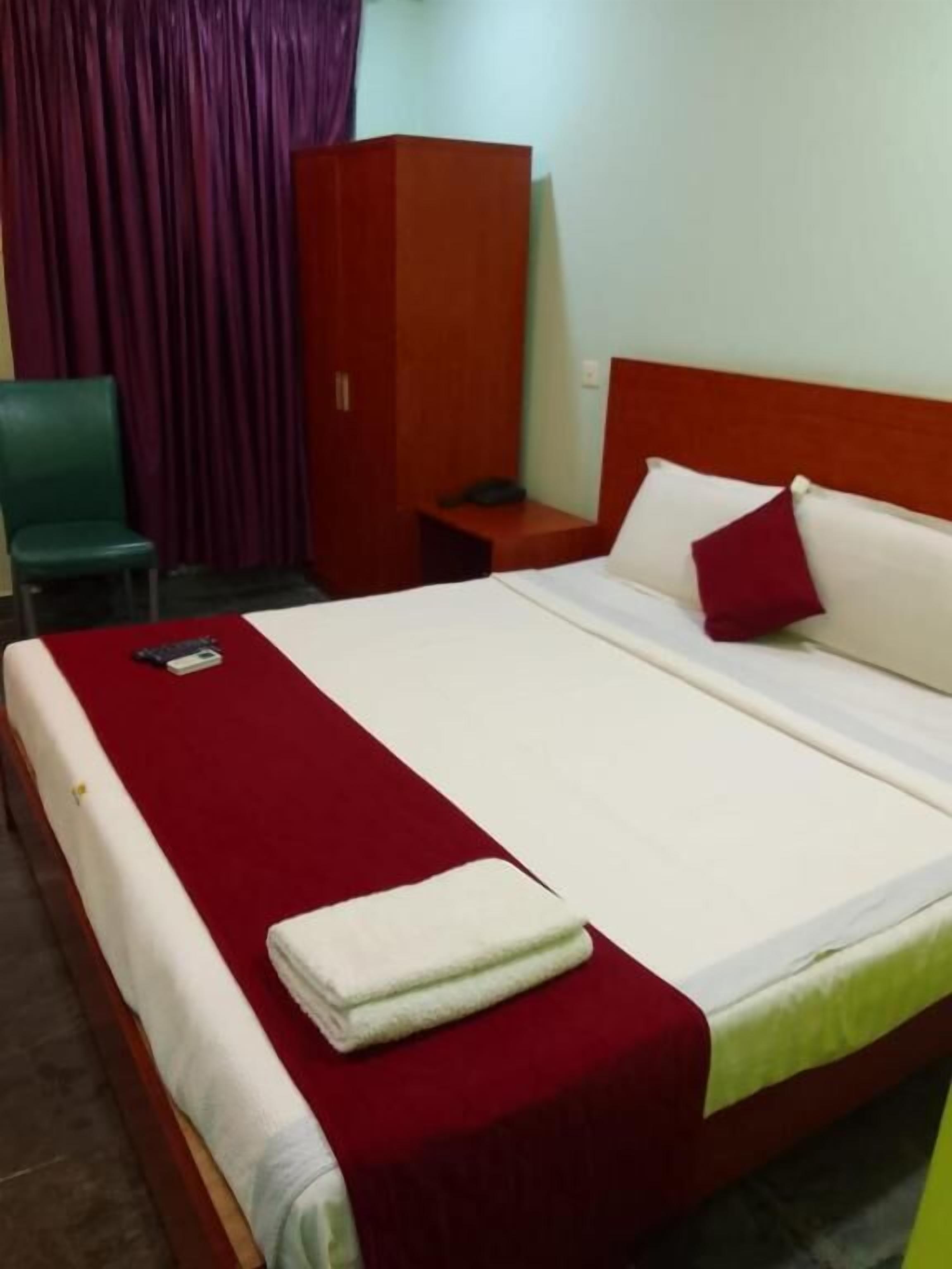 A hotel room with a bed, a nightstand, a chair, and a wardrobe.