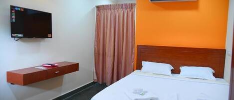 A hotel room with a bed, a TV mounted on the wall, a wooden headboard, and an air conditioning unit.