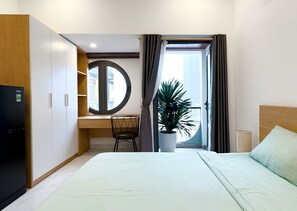 Habitación de hotel con cama, escritorio, silla, planta en maceta y vista al exterior.