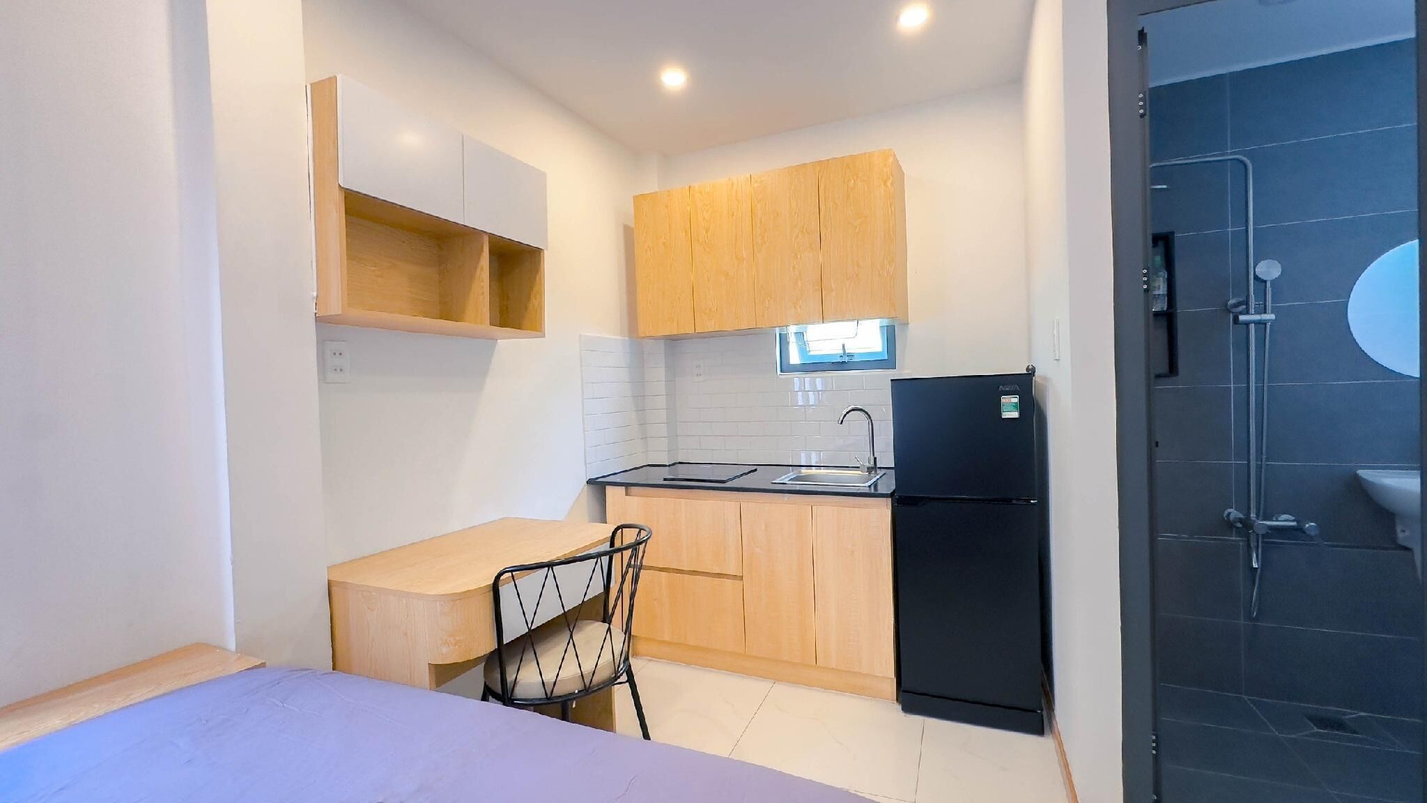 A compact kitchen with a sink, a black refrigerator, wooden cabinets, and a chair.