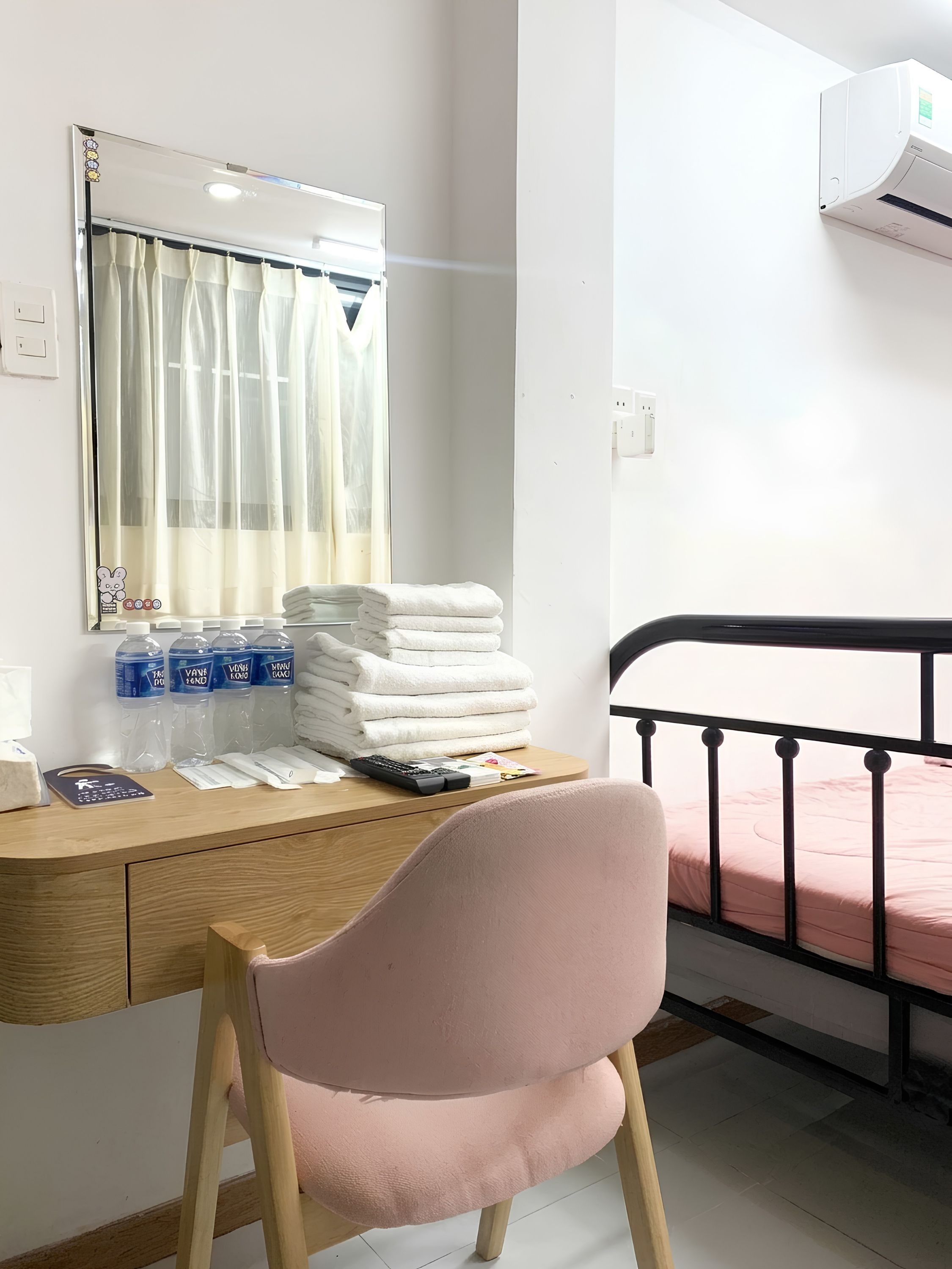A bedroom with a bed, a desk with a chair, a mirror, and a window with curtains.