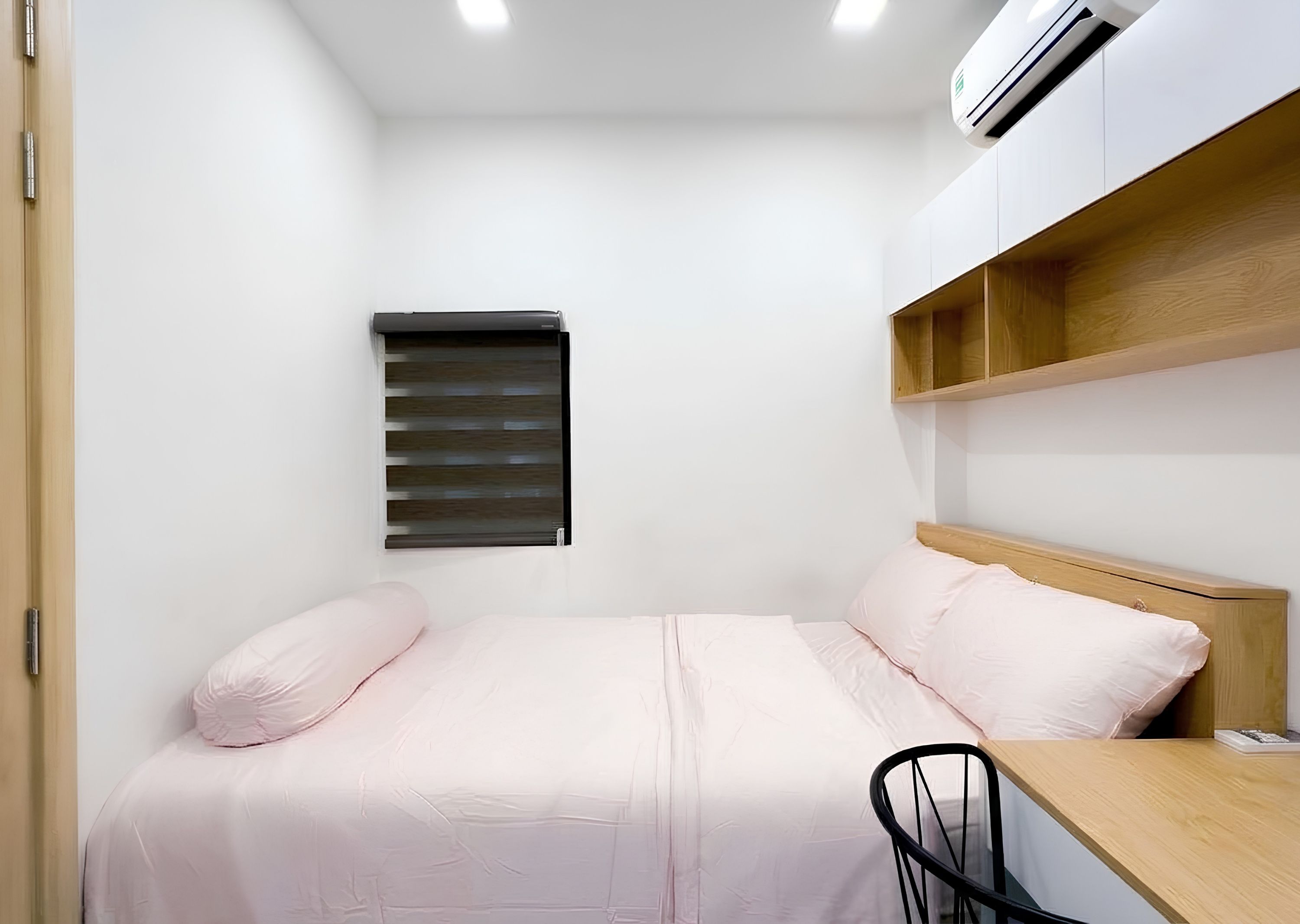Une petite chambre à coucher, bien rangée, avec un lit, un bureau et une fenêtre équipée de stores.