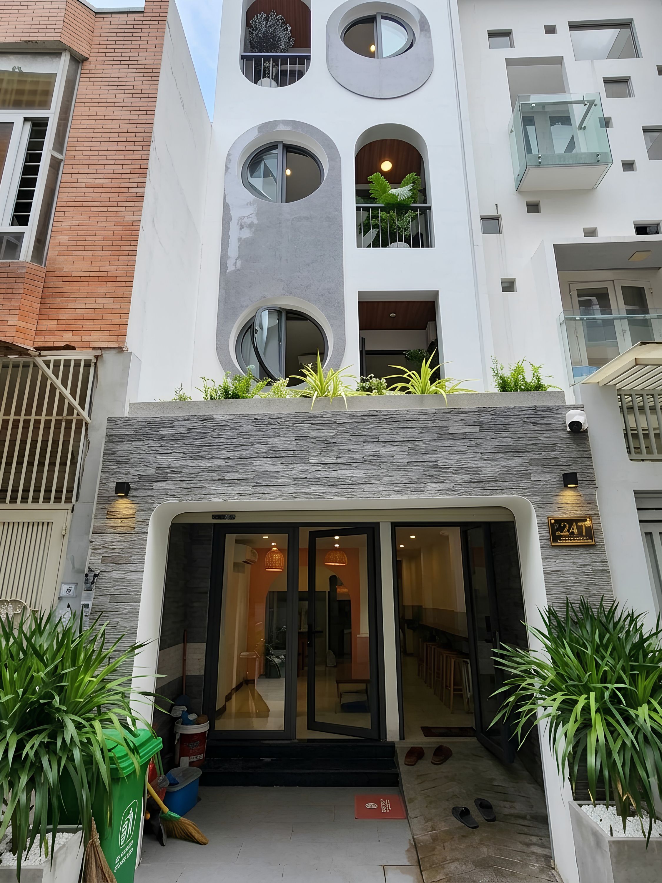 A modern building with a glass entrance, a stone facade, and a balcony with plants.
