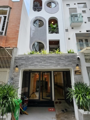 A modern building with a glass entrance, a stone facade, and a balcony with plants. - Lunaria Maison - Saigon Local, District 3 (Ho Chi Minh City)