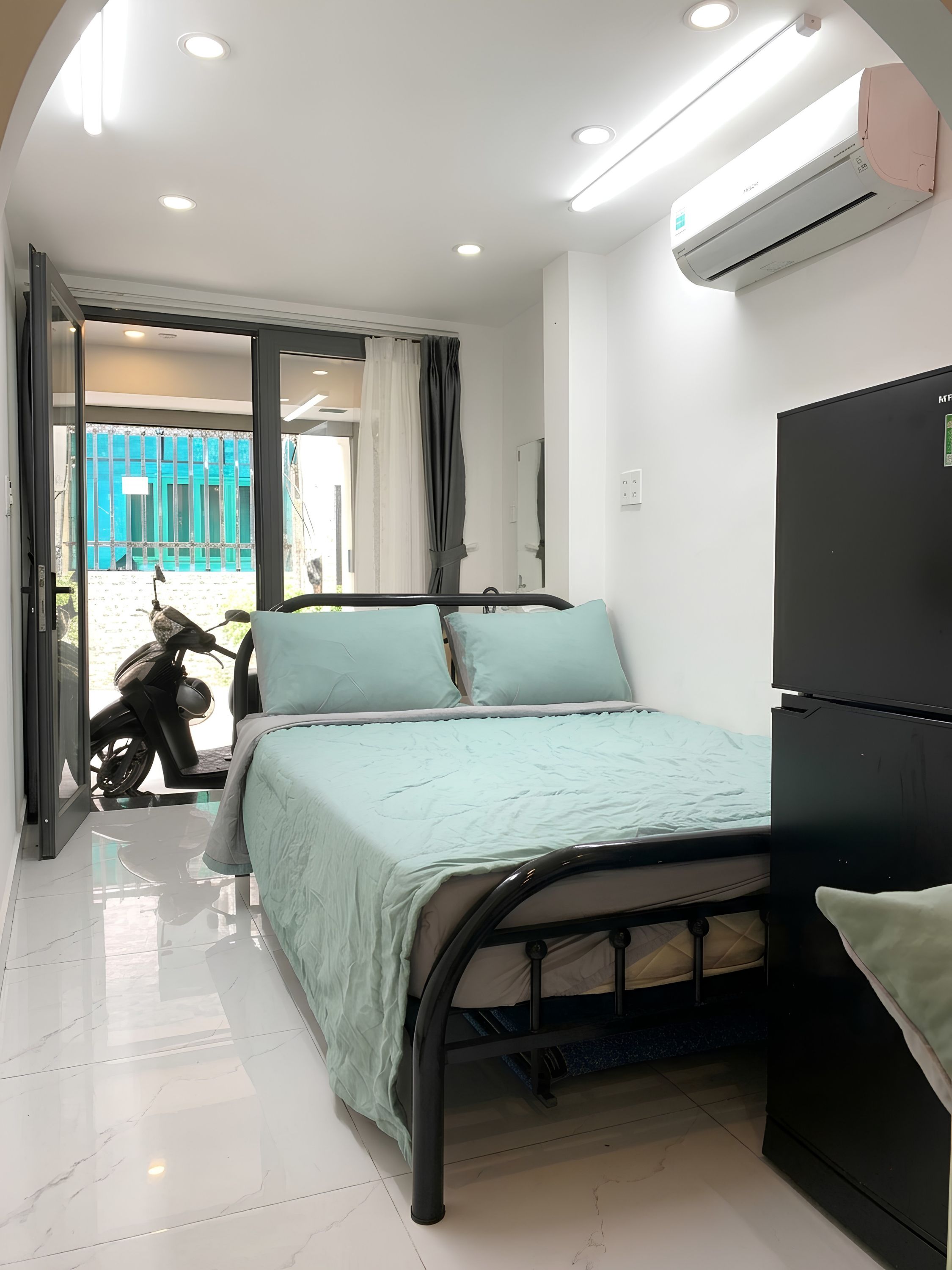 A bedroom with a bed, a black wardrobe, and an air conditioning unit.
