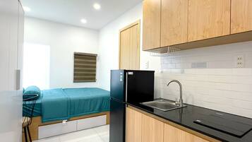 A compact kitchenette with a black refrigerator, wooden cabinets, a sink, and a window with blinds.