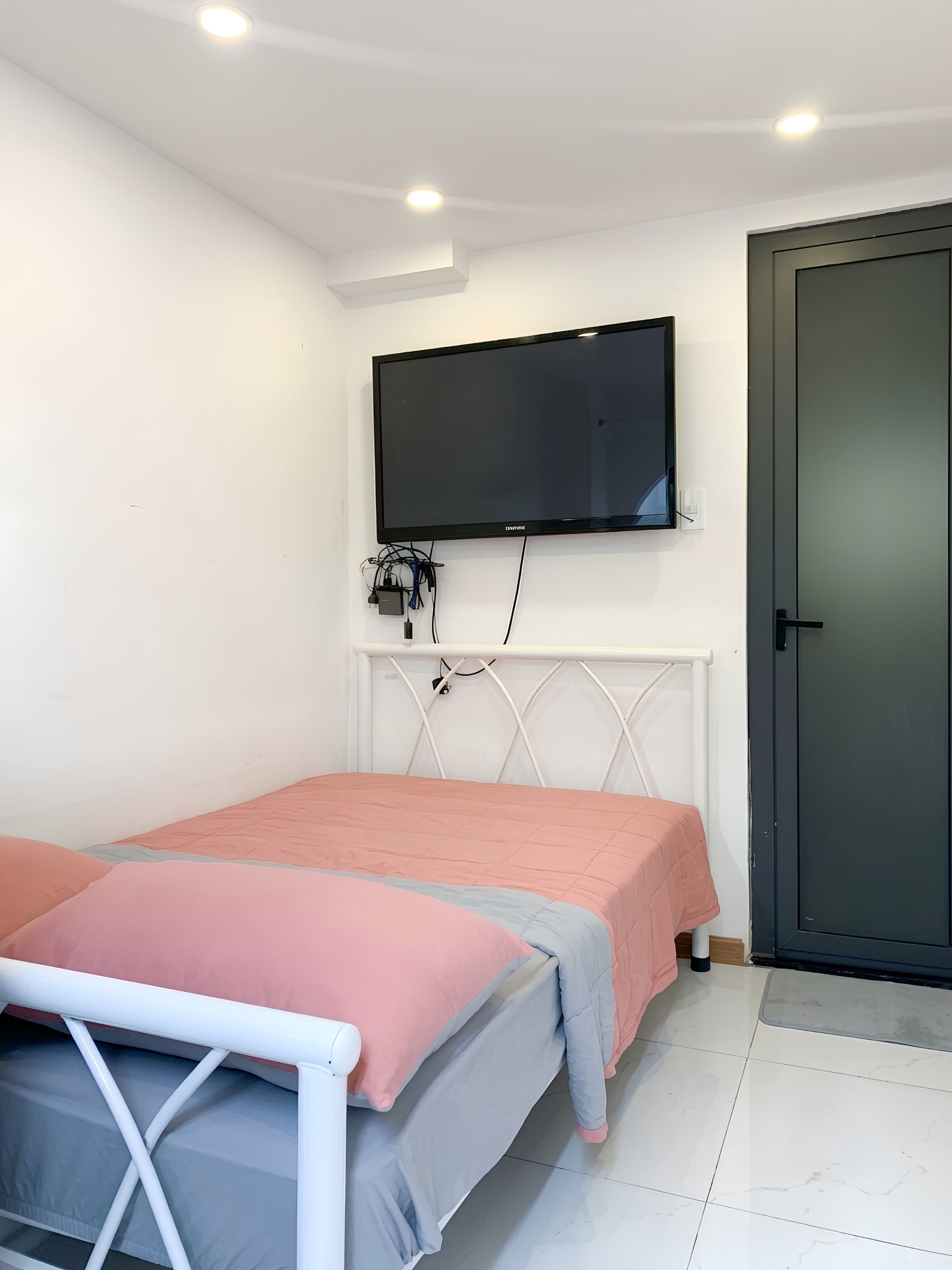 Une chambre à coucher avec un lit, un téléviseur fixé au mur et une porte.