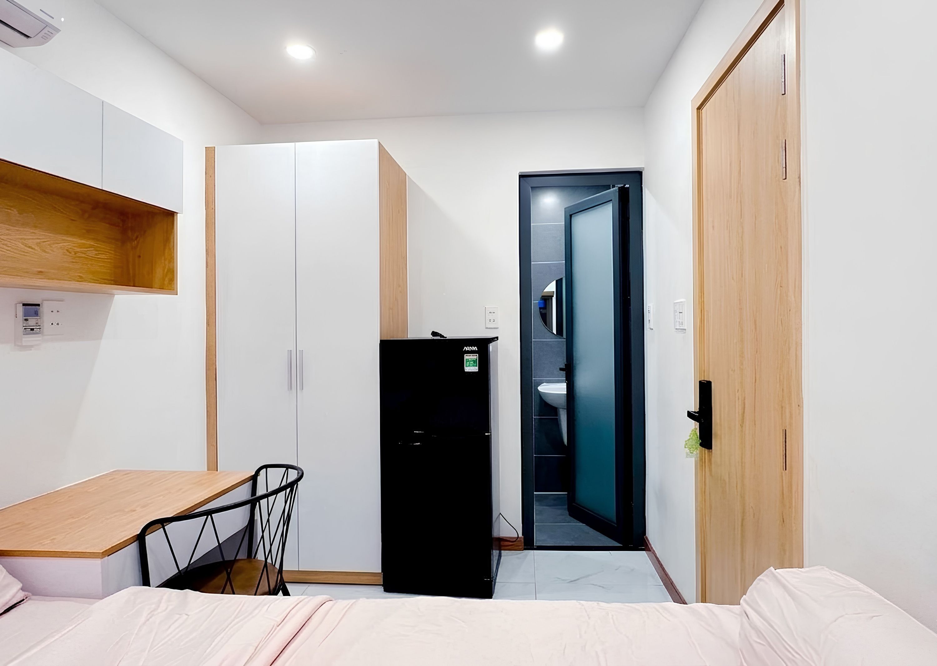 A compact room with a bed, a desk, a wardrobe, and a door leading to a bathroom.