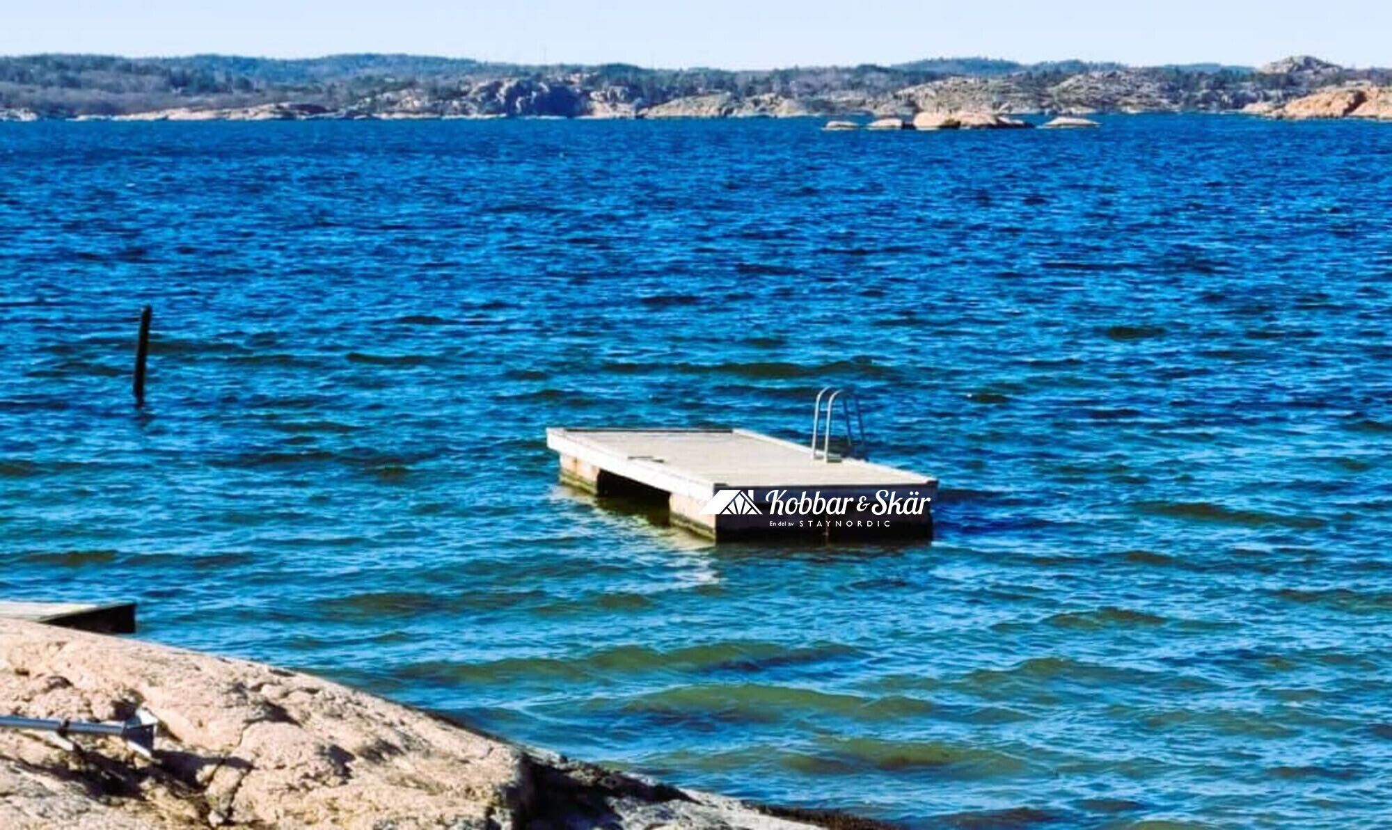 A boat named 'Kobbar & Skär' docked at a pier with a rocky shoreline in the background.