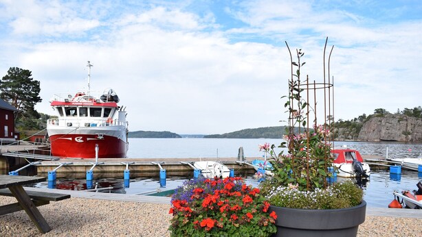 Un port où est amarré un bateau rouge et blanc, avec une table de pique-nique et des jardinières fleuries.
