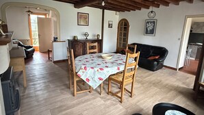 A cozy living room with a wooden ceiling, a dining table with a floral tablecloth, a black leather sofa, and a small round table with a decorative plate.