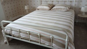A bed with a metal frame and striped bedding, a bedside table with a lamp, and a patterned wallpaper.