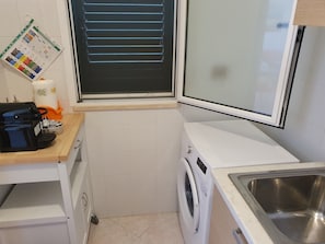 A compact kitchen with a washing machine, a sink, and a window with blinds. - Cozy vacation home with private pool 5 minutes from the beach (Torre dell'Orso)