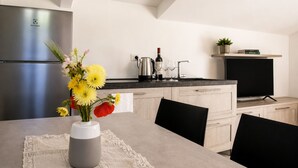 A modern kitchen with a refrigerator, a dining table with chairs, a vase of flowers, a coffee maker, wine glasses, and a television on a shelf. - Michelangelo Apartment (Toscana)