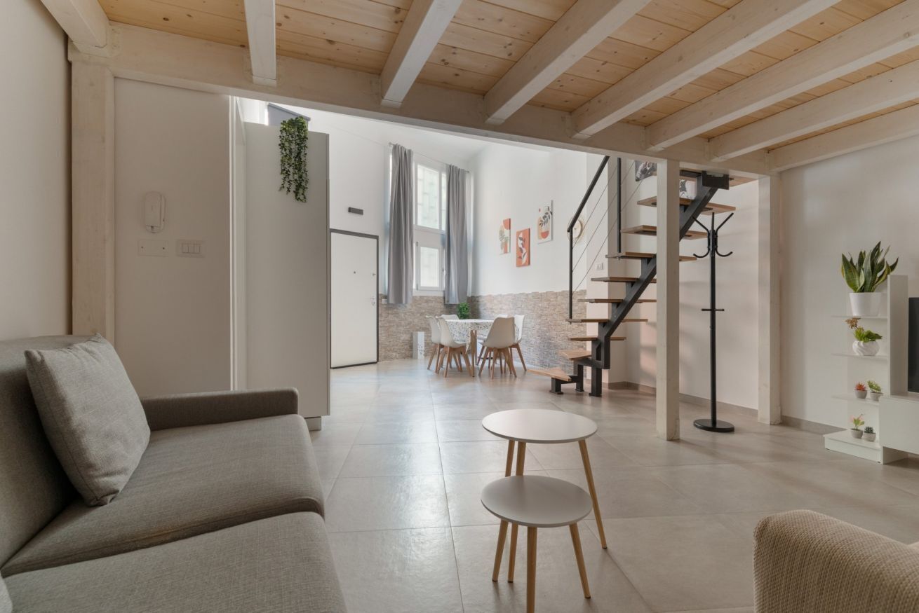 A modern living room with a sofa, a dining area with chairs, a staircase, and a plant.