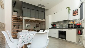 A modern kitchen with white cabinets, a black oven, and a microwave. There is a dining area with a table and chairs. - GuestHost - A comfortable and welcoming 56 square meters studio apartment, perfect for five people, located on the ground floor of a building with a private entrance.The property is located in the Affori neighborhood, an area full of amenities, including (Milan)