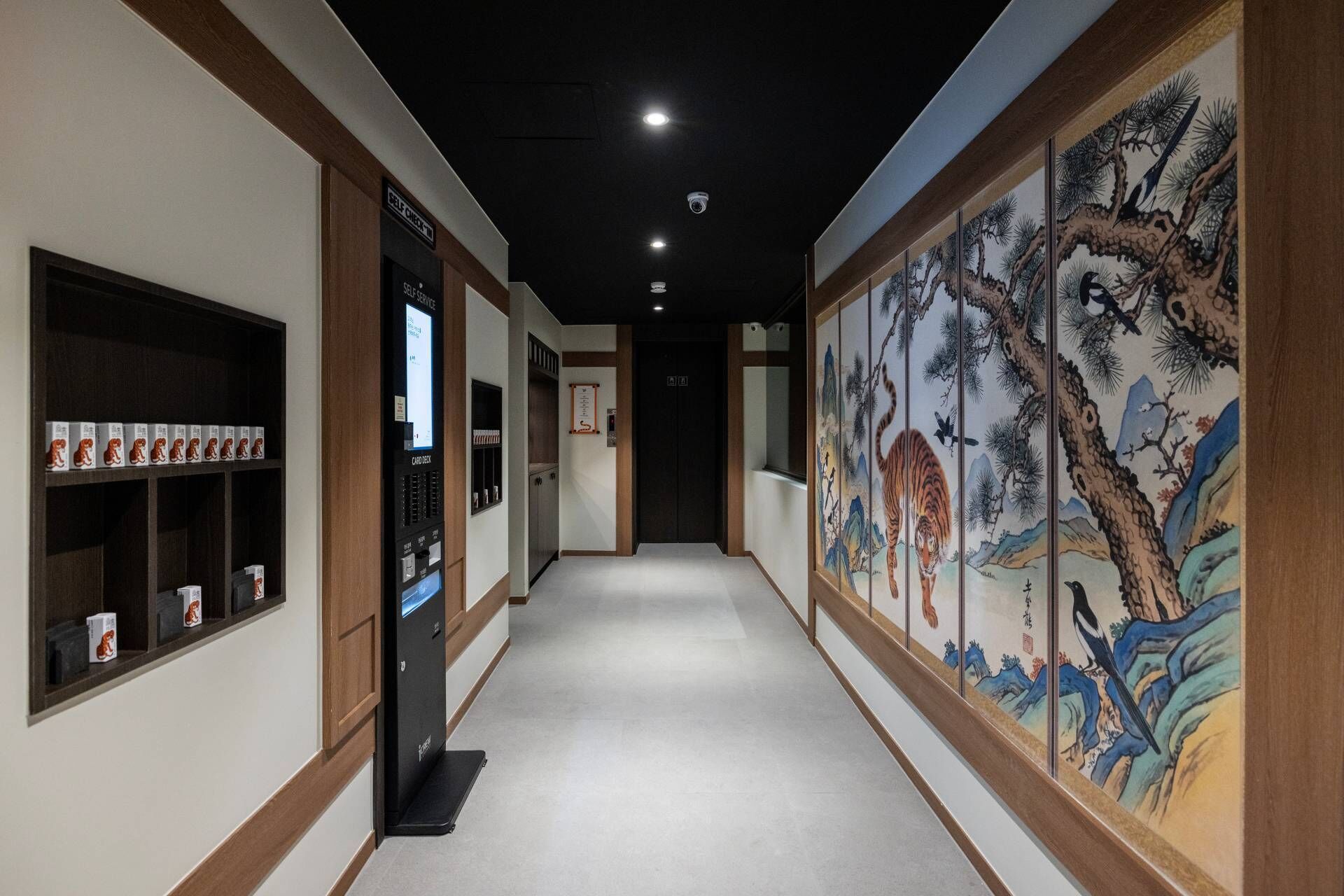 A hallway with a self-check-in kiosk, a card deck, and traditional artwork on the walls.
