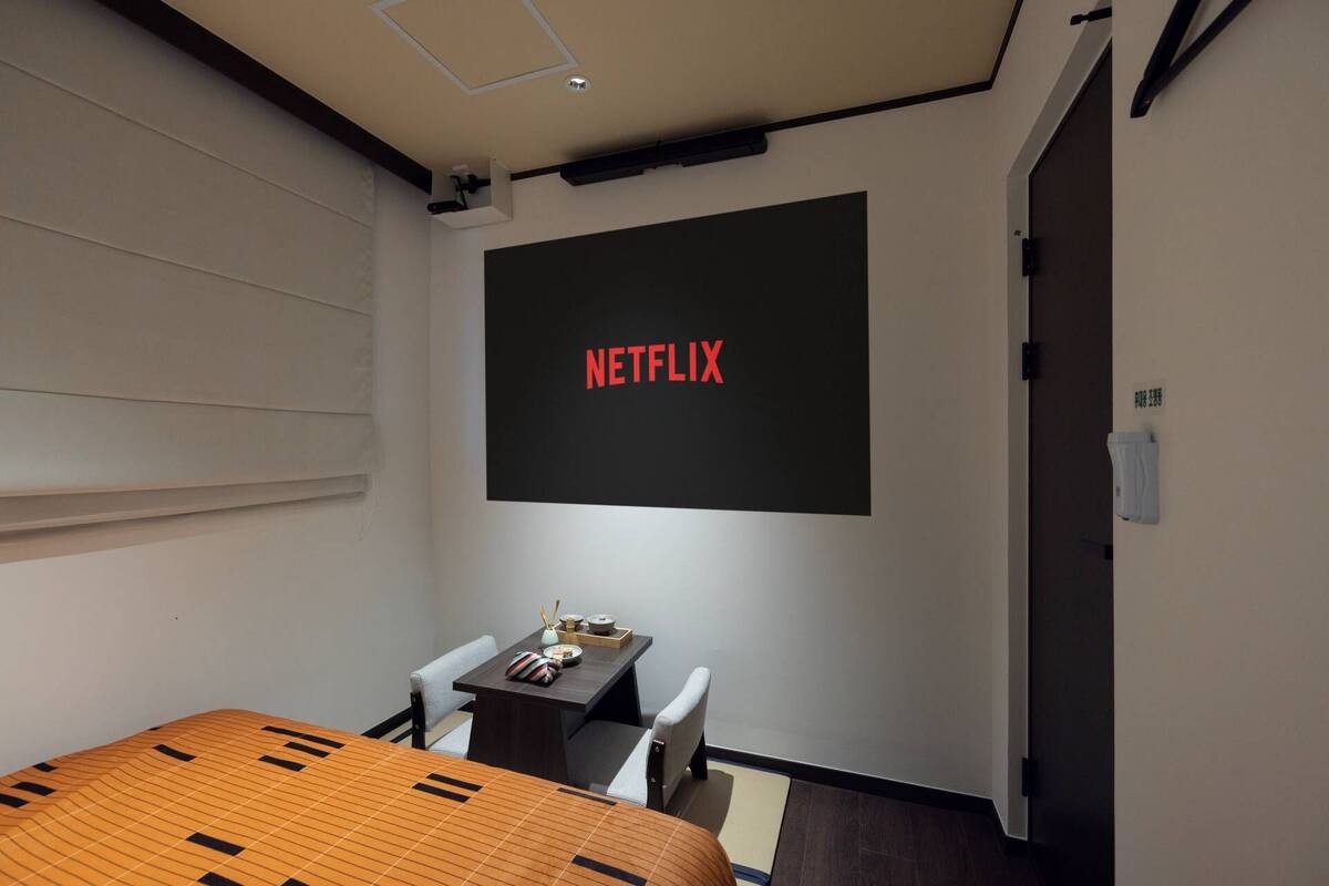 Ett litet rum med en säng, ett skrivbord och en väggmonterad skärm som visar texten ”NETFLIX”.