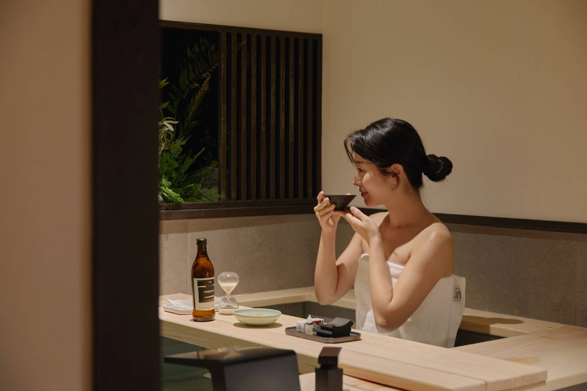 A person sitting at a table with a bottle, a bowl, and a small plate.