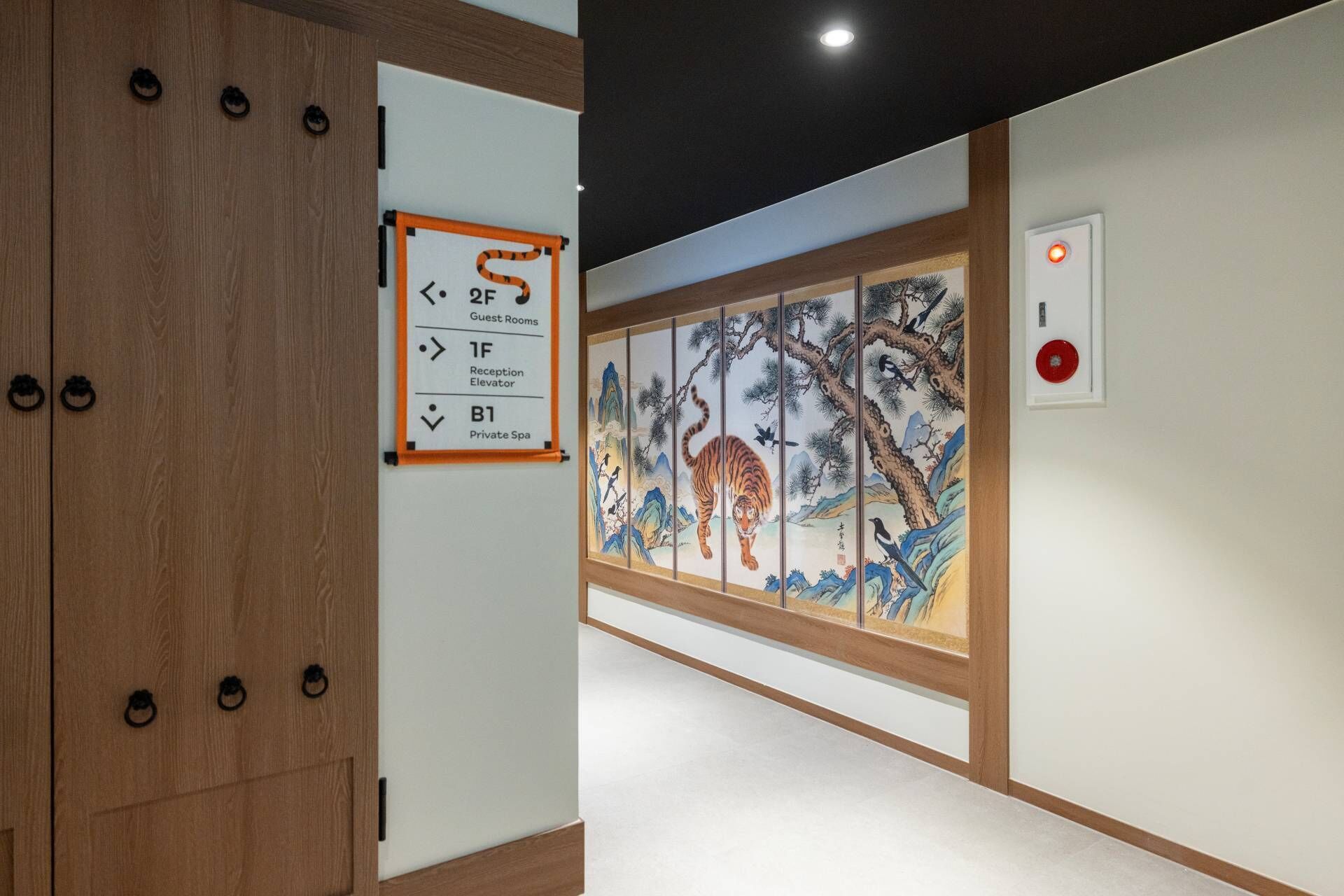 A hallway with a wooden door, a sign indicating guest rooms, a reception elevator, and a private spa.