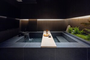 A modern spa area with a central hot tub, a wooden bench, and a bottle of water.
