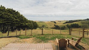 Een houten terras met twee Adirondack-stoelen met uitzicht op een glooiend landschap, een hek en bomen.