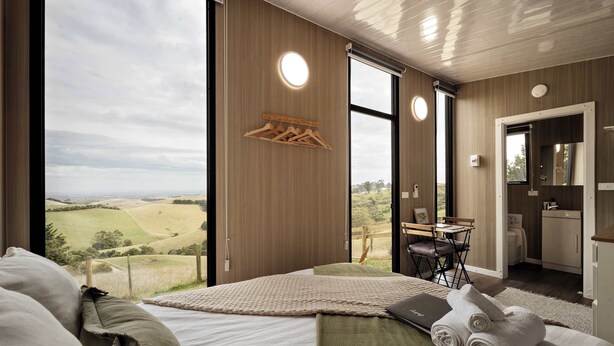 Een slaapkamer met een groot raam, een bed, een bureau en uitzicht op het platteland.