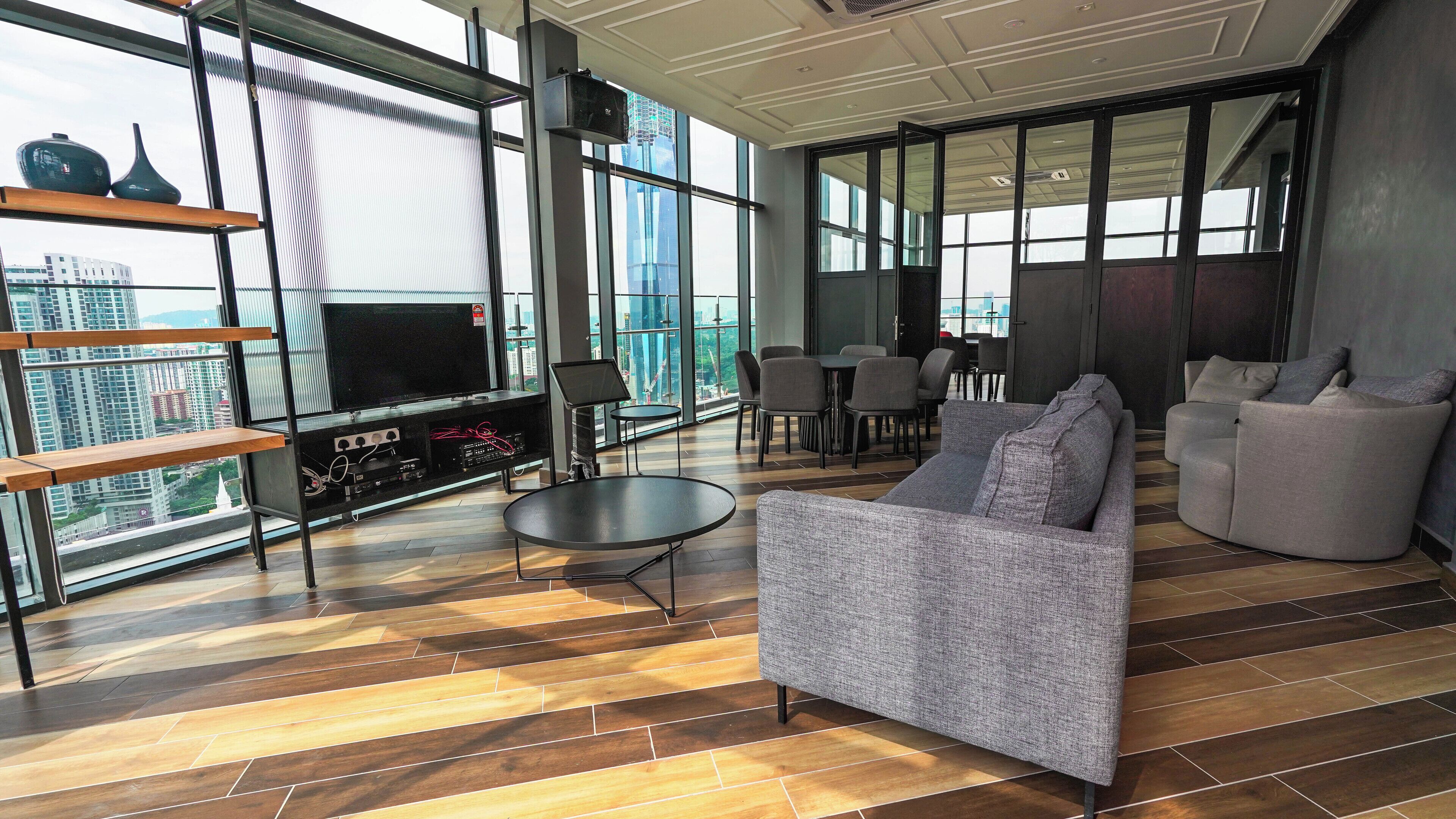 A modern living room with a sofa, a coffee table, and a TV. There is a balcony with a view of the city.