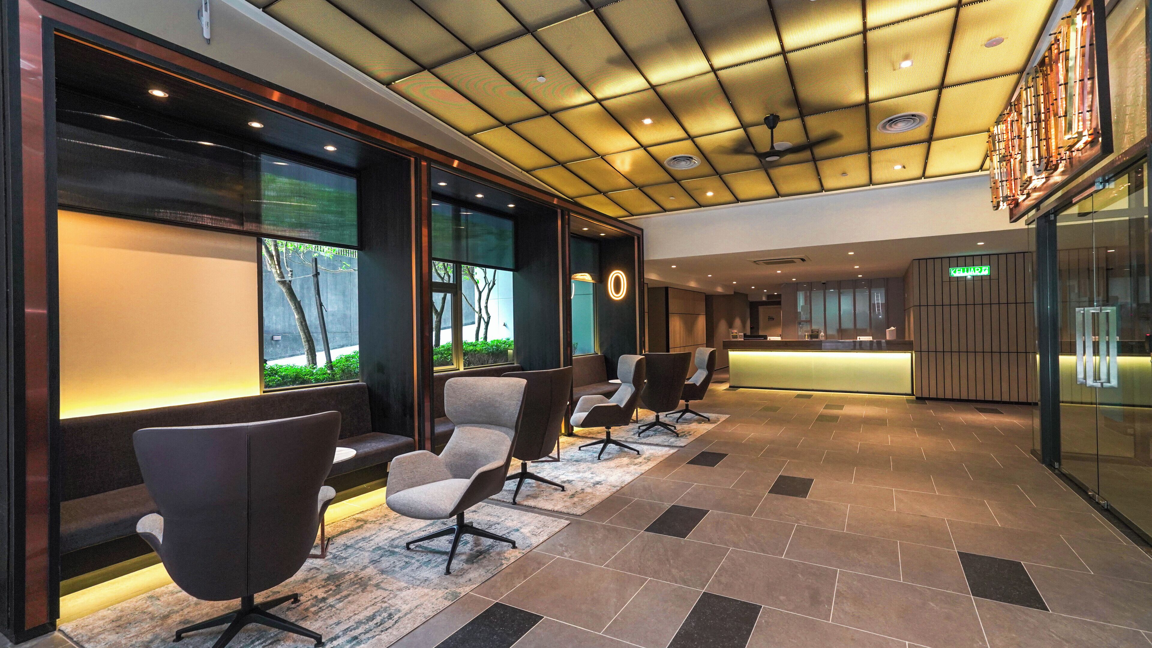 A modern hotel lobby with a reception desk, seating area, and a ceiling with recessed lighting.